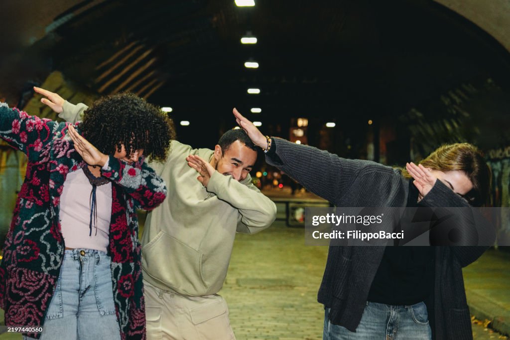 Three young friends dabbing under a bridge at night