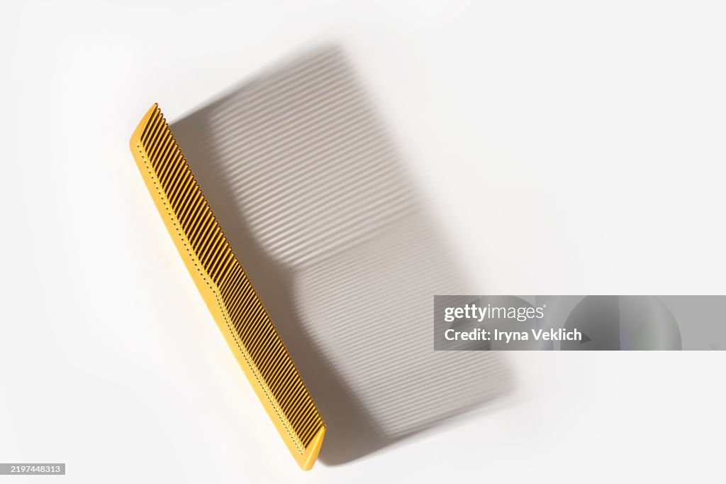 Trendy Beauty Product Gold Hair Comb with long shadow on white grey colour background. Routine step for healthy skin and hair care.