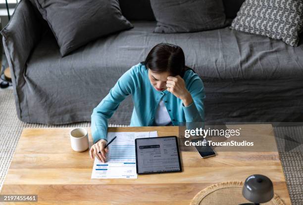 asian woman at home looking at bank statement and feeling anxious - cost of living stock pictures, royalty-free photos & images