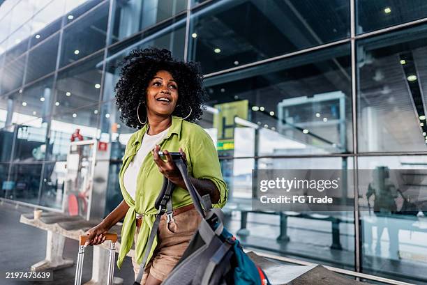 mid adult woman using mobile phone and looking around on a airport - reisbestemmingen stockfoto's en -beelden