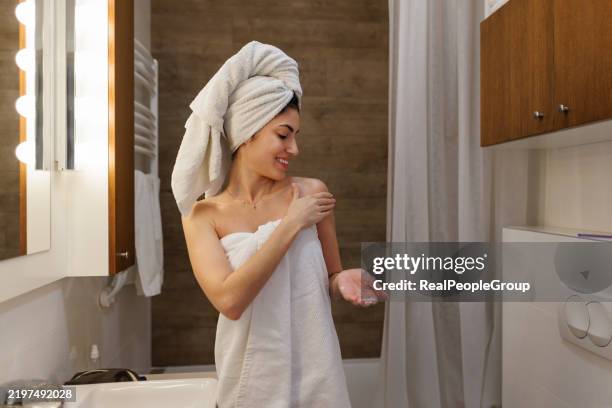 mujer joven que se aplica loción corporal después de la ducha en el baño - crema corporal fotografías e imágenes de stock