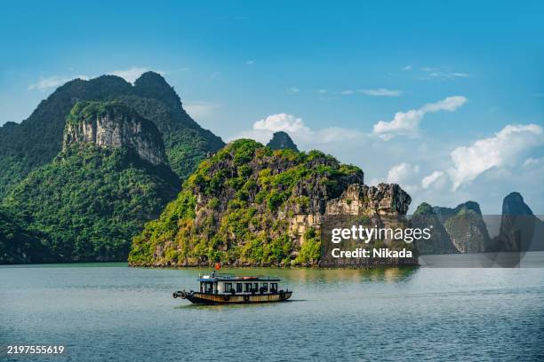 traditional boat passing limestone karsts in halong bay under clear blue sky - vietnam stockfoto's en -beelden