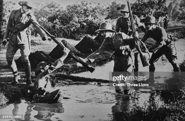 Troops of the Royal Netherlands East Indies Army crossing a drainage ditch during the Borneo campaign, 1945. A soldier holds out a helping hand to a...