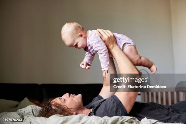 father lying on bed lifting baby daughter in the air - two girls holding hands in silhouette stock pictures, royalty-free photos & images
