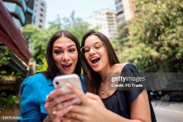 female friends using mobile phone in the street - scrolling stock pictures, royalty-free photos & images
