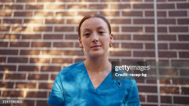 portrait of a nurse in blue scrubs against a brick wall - human role stock pictures, royalty-free photos & images