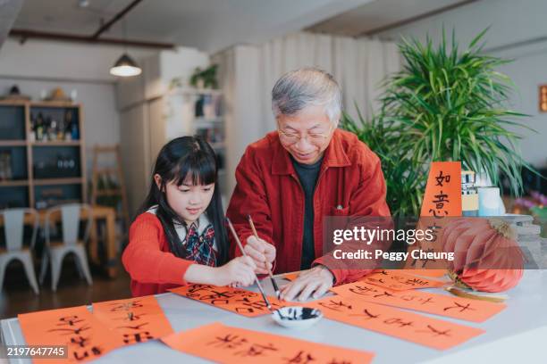 modern hong kong family celebrating chinese new year. grandparent is writing spring couplets with grandchild - orthographic symbol stock pictures, royalty-free photos & images