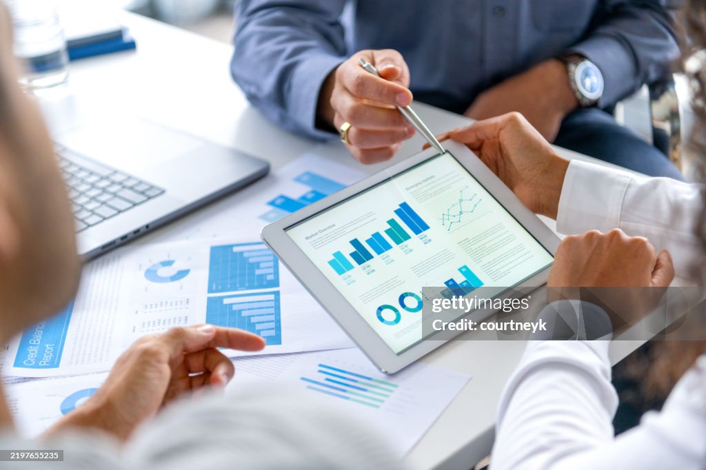Close up of three people looking at financial data with graphs and charts.