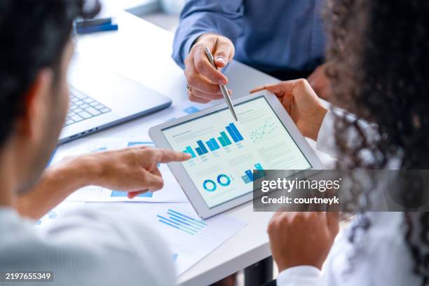 nahaufnahme von drei personen, die sich finanzdaten mit grafiken und diagrammen ansehen. - aktenmappe stock-fotos und bilder