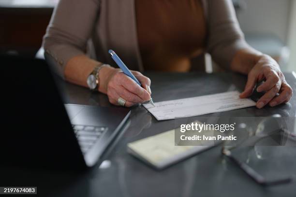woman signing a personal check on office desk near laptop - writing stock pictures, royalty-free photos & images