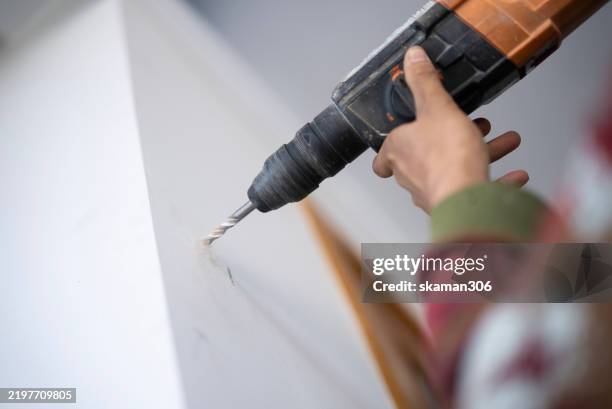 a worker operates a power drill to make a hole in a white wall, producing dust. the image captures home improvement work. - broca imagens e fotografias de stock