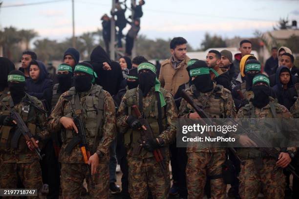 Hamas fighters stand in formation as Palestinians gather on a street to watch the handover of three Israeli hostages to a Red Cross team in Deir...