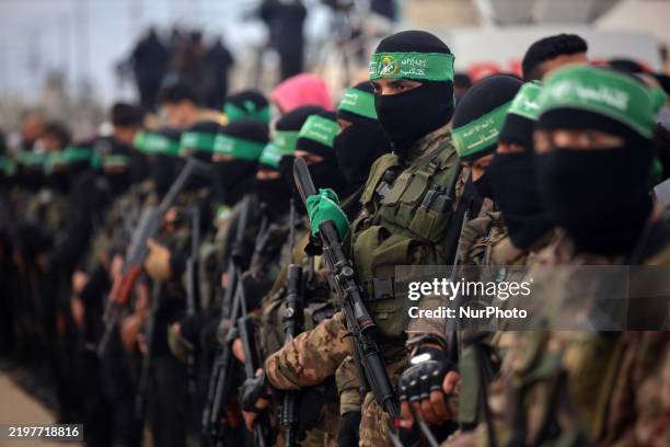 Hamas fighters stand in formation as Palestinians gather on a street to watch the handover of three Israeli hostages to a Red Cross team in Deir...