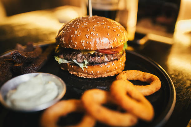 tasty beef burger with lettuce, cheese and tomato, onion rings and garlic sauce - grill cafe stock pictures, royalty-free photos & images