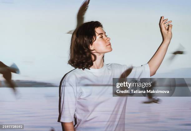 a woman dreamer against a white wall and a projection of flying birds on her and the wall - stopschild stock-fotos und bilder