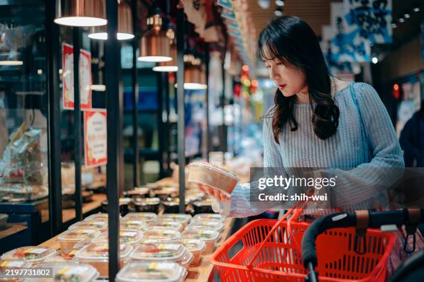 an asian woman is using her smartphone while enjoying a meal at a restaurant. she completes her online food order through the tech device and settles the payment with a digital wallet. this is a blend of people, food, lifestyle, and technology. - bento box stock pictures, royalty-free photos & images
