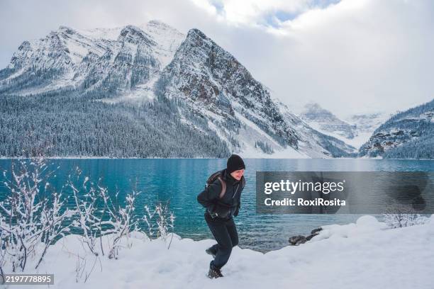 hiker walking between snowy mountains and turquoise lake in banff canada - banff ski stock pictures, royalty-free photos & images