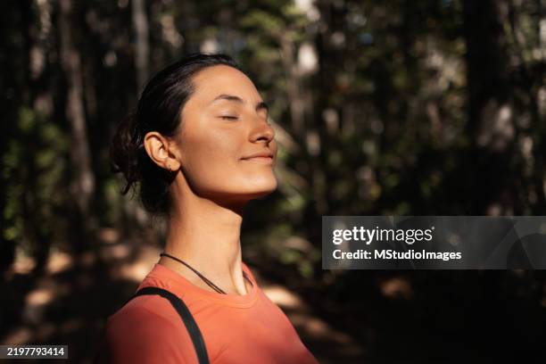 donna che gode della luce del sole nella natura con espressione serena, indossando abbigliamento casual - medicina alternativa foto e immagini stock