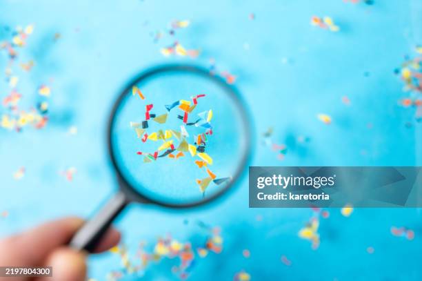hand with magnifying glass revealing microplastic particles on surface of blue water - mikroplastik stock-fotos und bilder