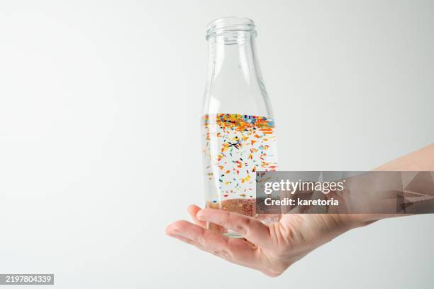 hand holding glass bottle with floating microplastic particles in water - mikroplastik stock-fotos und bilder
