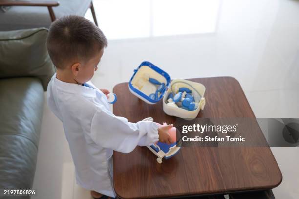 junger junge als arzt mit spielzeugartigen medizinischen werkzeugen beim spielen - rollenspiel stock-fotos und bilder