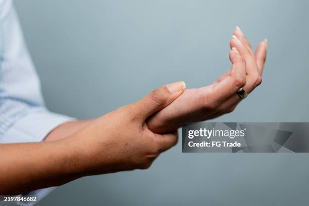 close-up of a woman massaging her wrist on a gray background - wrist stock pictures, royalty-free photos & images