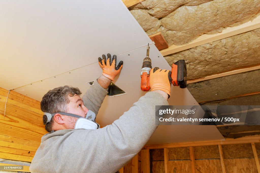 Construction worker installs drywall in interior space using power