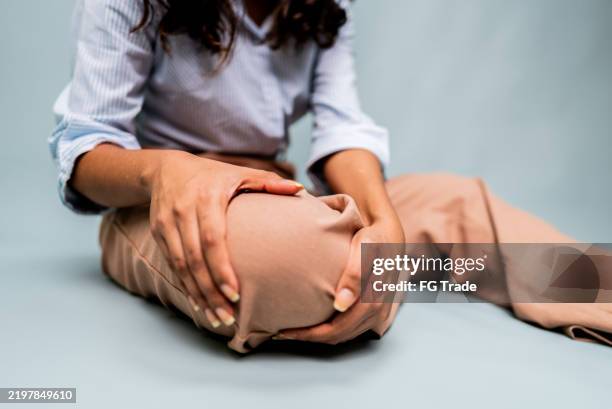nahaufnahme einer frau, die ihr knie auf grauem hintergrund massiert - gelenkrheumatismus stock-fotos und bilder