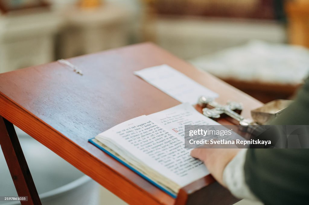 Priest reading holy book during church ceremony with silver cross