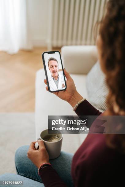 woman using phone talk to doctor sitting on sofa - online therapy stock pictures, royalty-free photos & images