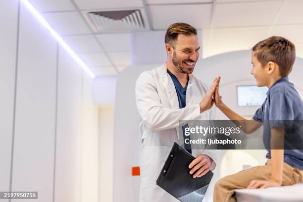 doctor high-fiving young boy during friendly medical appointment in radiology room - free health screening stock pictures, royalty-free photos & images