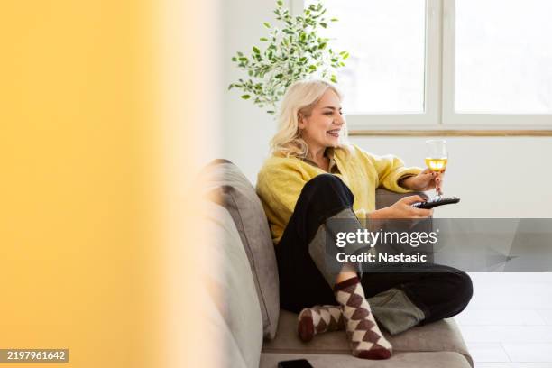 lächelnde mittlere erwachsene frau, die mit der fernbedienung den kanal wechselt - smart tv stock-fotos und bilder