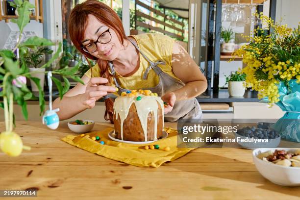 redhead woman decorating traditional easter cake with colorful chocolate eggs. easter treat. - cake-decorating stock pictures, royalty-free photos & images