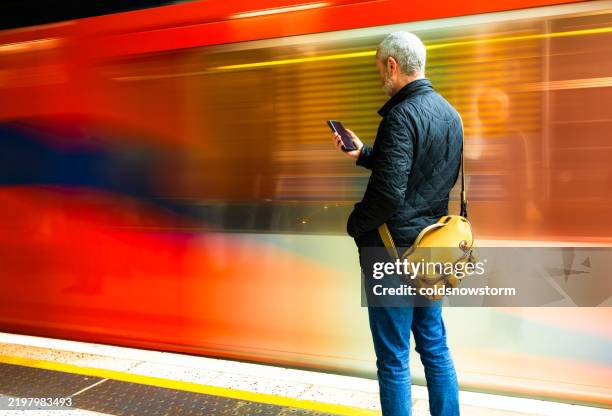 mid adult male commuter looking at smart phone with speeding train motion blur - station stock pictures, royalty-free photos & images