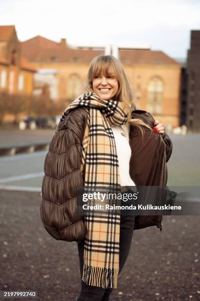 Jeanette Madsen wears black jeans, white Rotate top, brown textured leather jacket from Rotate, beige white and black checkered scarf outside the...