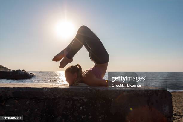 silhouette stretches against glowing horizon at coastal pier. athlete demonstrates scorpion backbend during seaside sunset practice - contortionist stock pictures, royalty-free photos & images