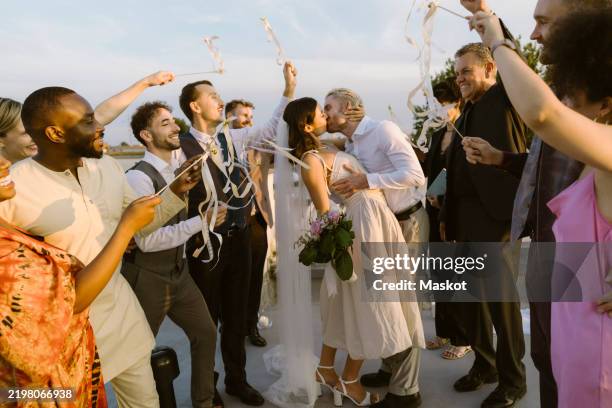 guests cheering newly married couple kissing each other on rooftop - cérémonie du mariage photos et images de collection
