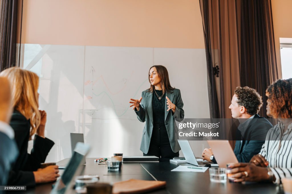 Female business entrepreneur explaining strategies to colleagues in board room at office