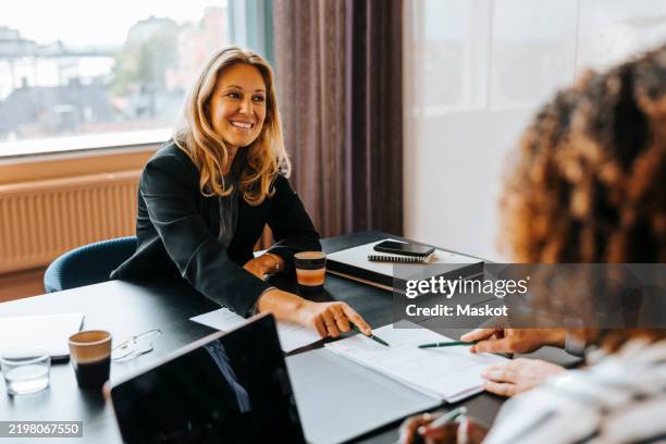 happy female entrepreneur pointing at agreement while discussing with clients at office - hand sign stock pictures, royalty-free photos & images