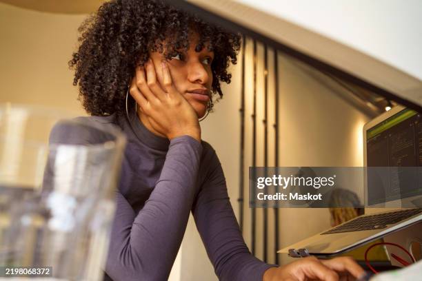low angle view of bored young it professional with curly hair leaning on elbow at desk in office - exclusion photos et images de collection