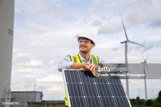 engineer inspecting solar panel with wind turbines under clear sky - energy storage stock pictures, royalty-free photos & images