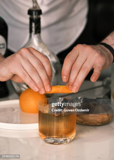 bartender garnishing a smoked whiskey cocktail with orange zest at an italian restaurant, luxury mixology with premium spirits and aromatic citrus, craft cocktail presentation in a sophisticated bar setting - liqueur stock pictures, royalty-free photos & images