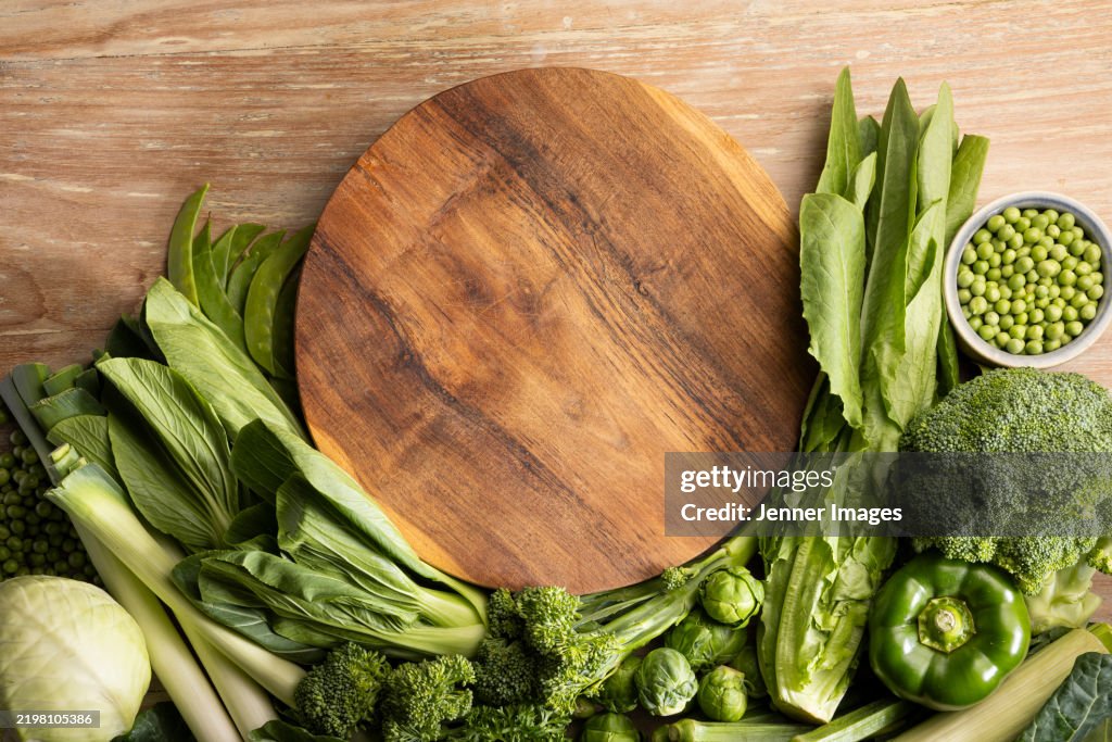 Abundance of fresh green vegetables on a light wood background.