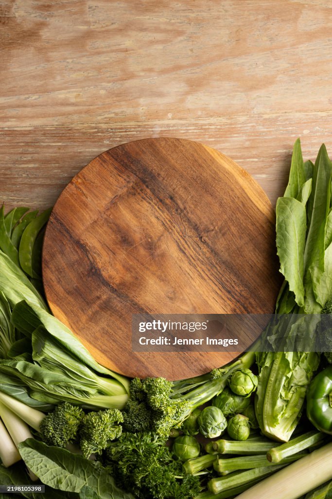 Abundance of fresh green vegetables on a light wood background.