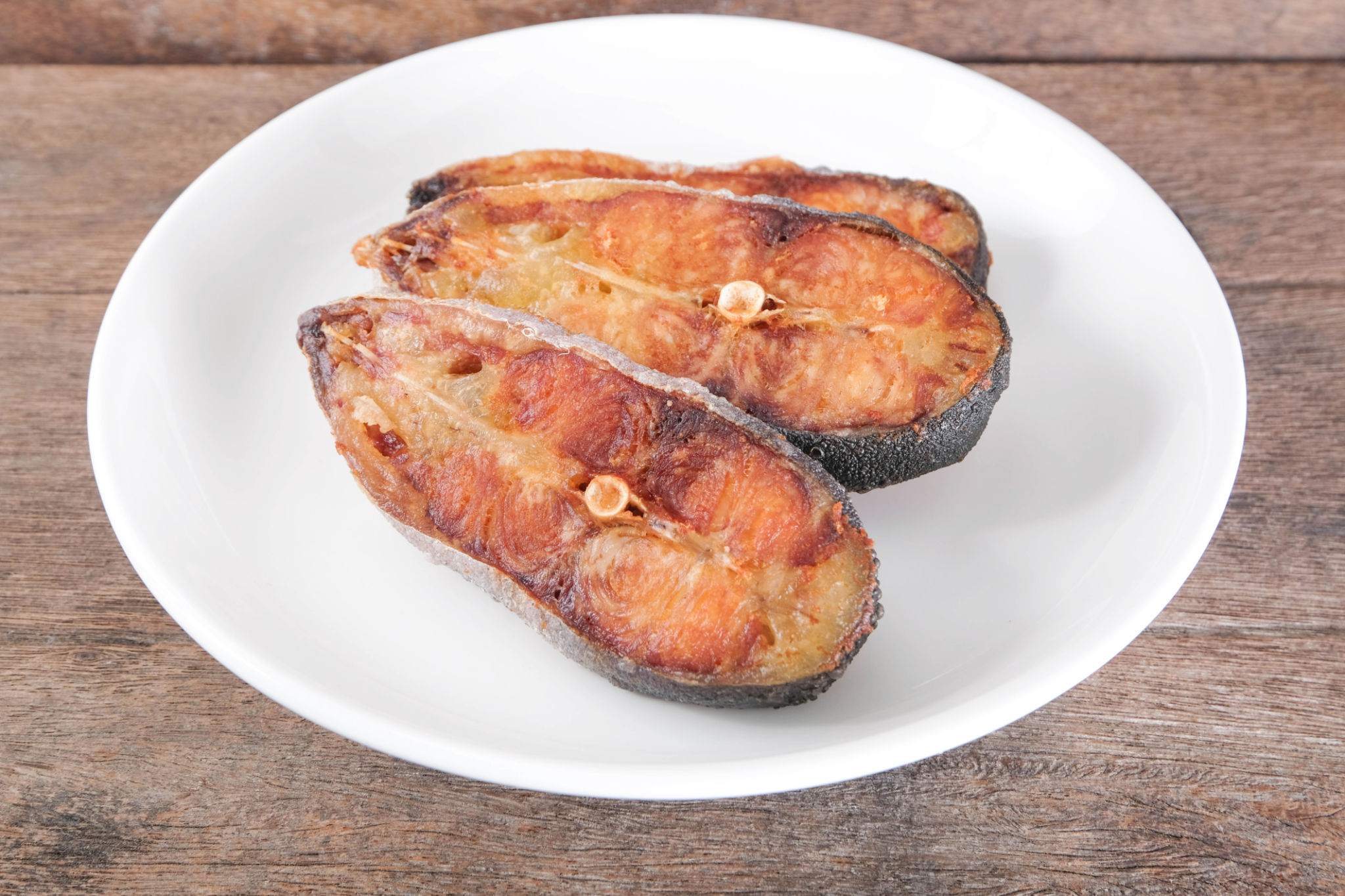 Sun-dried pangasius in a white ceramic plate on a wooden table. Sun-dried pangasius in a white ceramic plate on a wooden table.