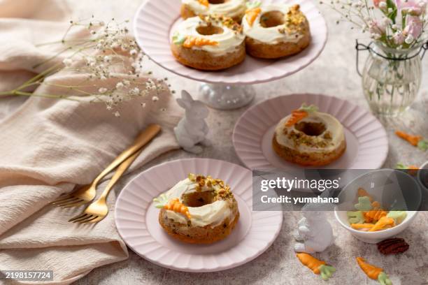 delicious carrot cake donuts with cream cheese frosting decorated with little chocolate carrots on gray concrete background for festive dinner. - sponge cake stock pictures, royalty-free photos & images