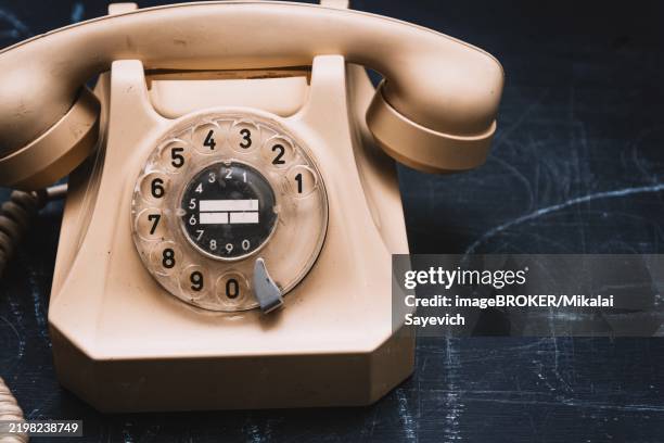 close-up of a beige vintage rotary phone on a dark surface, evoking a sense of nostalgia - close up phone on surface stock-fotos und bilder