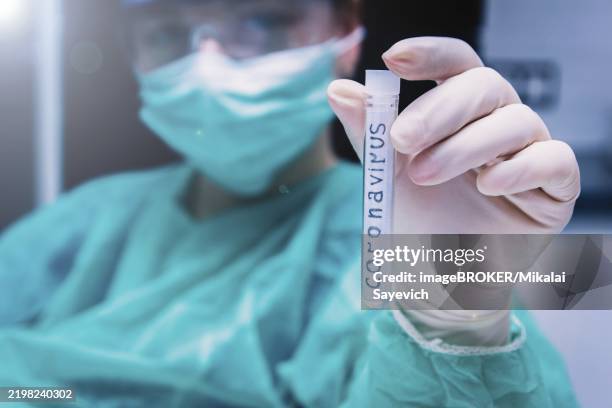 close-up of a hand holding a coronavirus test tube, with a health worker in protective clothing in the background - lateral flow test stock pictures, royalty-free photos & images