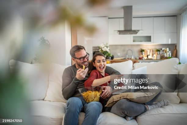 young couple resting at home, spending a relaxed weekend together watching an online movie - subscription stock pictures, royalty-free photos & images