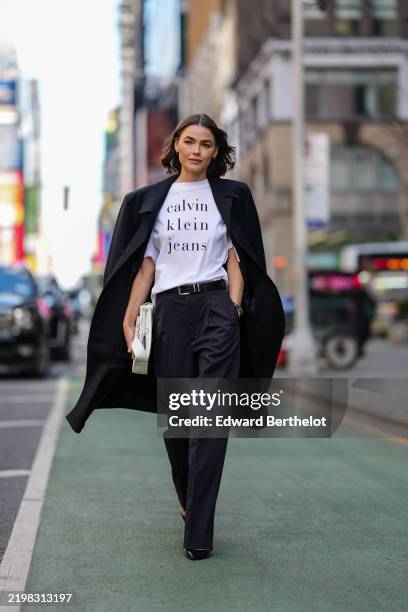 Bambi Northwood Blyth wears white oversized Calvin Klein jean print shirt, black oversized coat, shiny black leather belt, black high waisted relaxed...